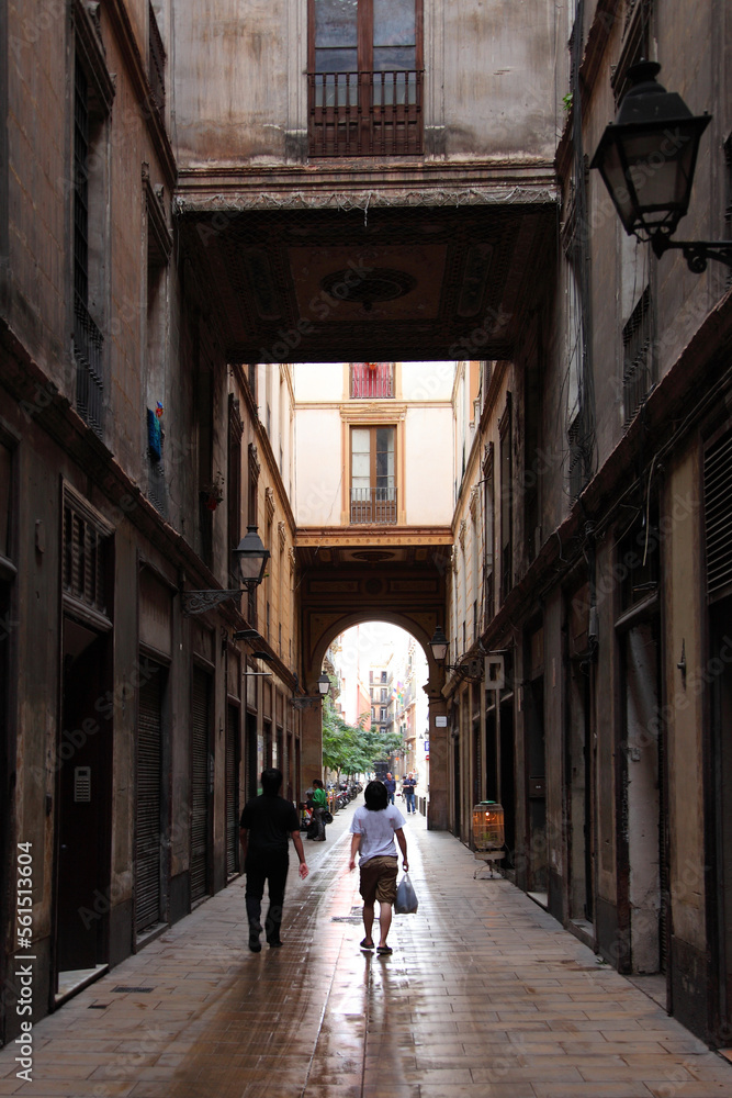 Narrow street of the old city Barcelona lit by the sun and houses in the shade.