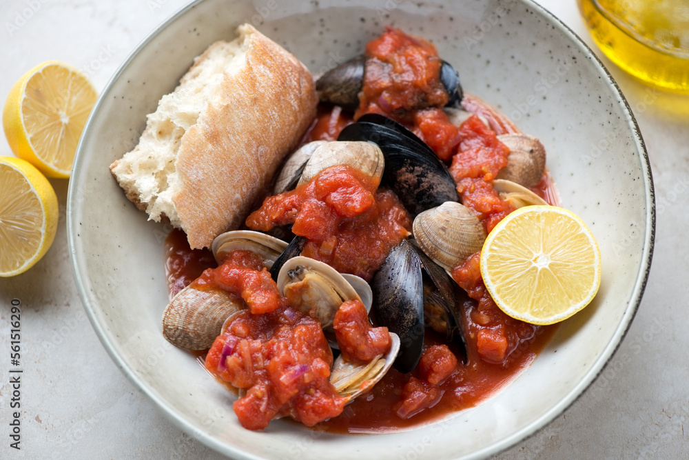 Beige plate with steamed mussels and littleneck clams in thick tomato broth, middle closeup, horizontal shot, selective focus Beige plate with steamed mussels and littleneck clams in thick tomato broth, middle closeup, horizontal shot, selective focus