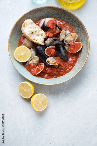 Plate of tomato broth with mussels and vongole on a light-grey granite background, vertical shot with copyspace, flat lay
