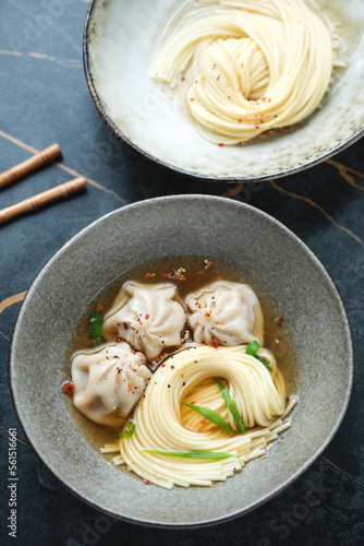 Bowl of wonton soup with egg noodles on a dark-olive marble background, vertical shot, elevated view