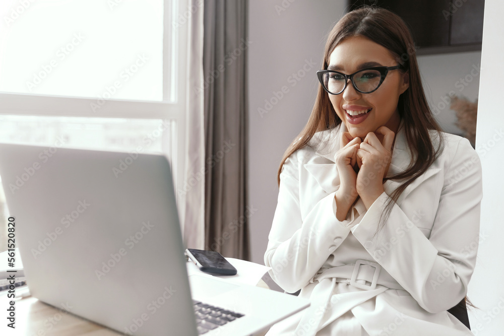 Beautiful happy young businesswoman, woman using laptop and smiling while working indoors Beautiful happy young businesswoman, woman using laptop and smiling while working indoors
