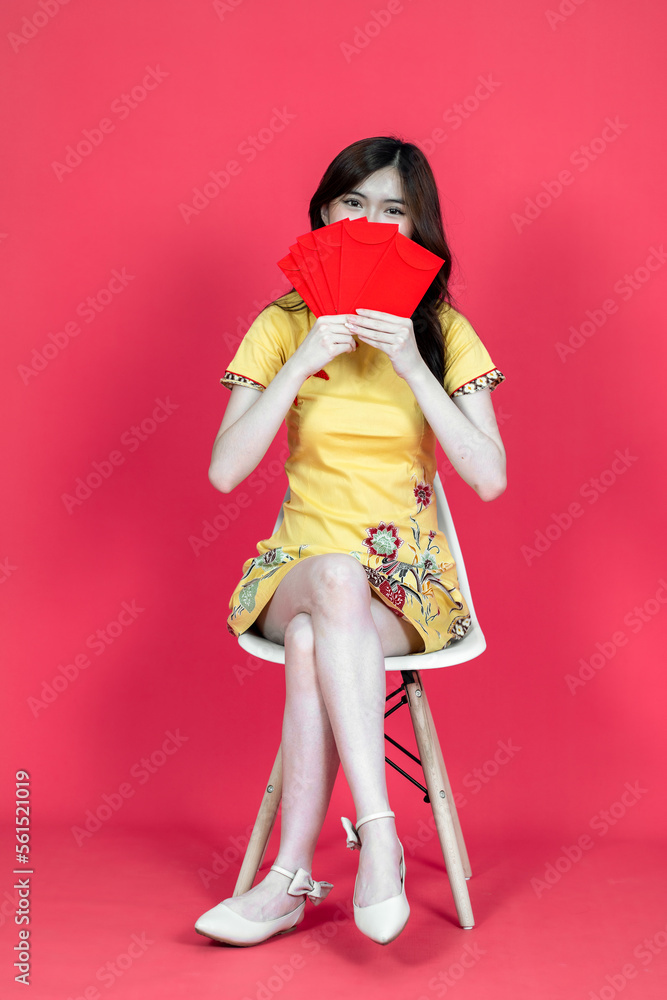 A beautiful asian woman sitting and holding some hongbao red envelopes while wearing simple yellow chinese dress