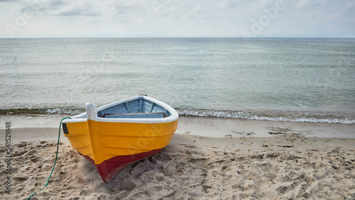 Fototapeta Naklejka Na Ścianę i Meble -  A small yellow fishing boat on the shore of a beach on the Baltic Sea in Poland