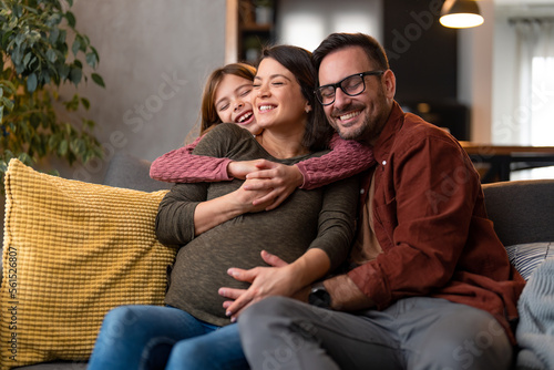Happy young family having good time together, sitting on a couch in the living room, embracing, bonding and smiling with the eyes closed.