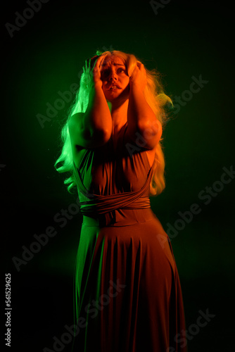portrait of pretty girl with blonde hair & elegant gown with expressive facial expressions & gestural arm poses. colourful neon gel lighting, isolated on black studio background.