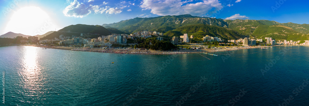 Panorama of beach with sun umbrellas, sunbeds and people relaxing in the town of Becici near Adriatic Sea against the backdrop of sunny sky