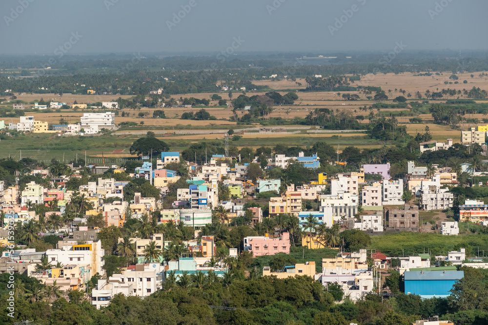 Aerial view of low rise buildings and houses surrounded by green farmland in the town of Trichy in Tamil Nadu, India.