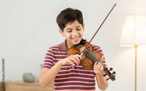 Photo Indian handsome teenage boy, smiling, playing, practicing violin musical instrument with happiness in bedroom at cozy home in leisure time, smiling, having copy space