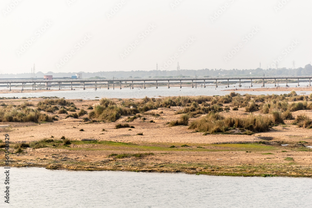 View of the sandy banks of an island in the Cauvery river in the town of Trichy with a bridge in the background. View of the sandy banks of an island in the Cauvery river in the town of Trichy with a bridge in the background.