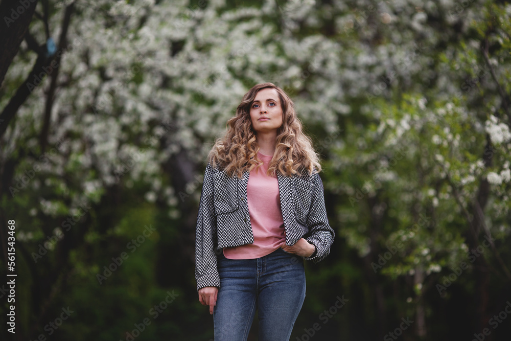 Confident woman in spring or summer nature against background of flowering trees. Model with long curly hair Confident woman in spring or summer nature against background of flowering trees. Model with long curly hair