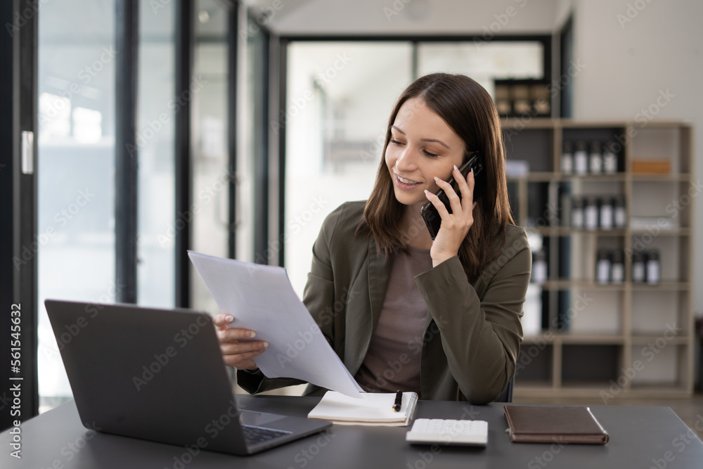 Happy young woman talking on the mobile phone and smiling while sitting at her working place in office. Happy young woman talking on the mobile phone and smiling while sitting at her working place in office.