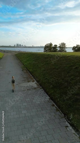 Vertical video: A person rides a scooter near the beach overlooking the city