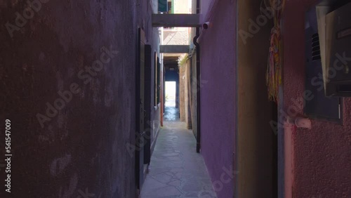 Narrow lane passage with shabby dark red walls with walkways and doors to enter inside and brightly illuminated way out in end in Burano photo