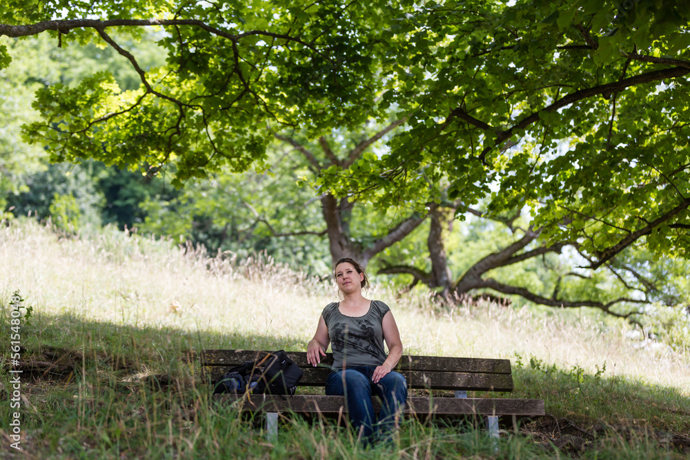brunette woman resting on bench in shade of trees brunette woman resting on bench in shade of trees