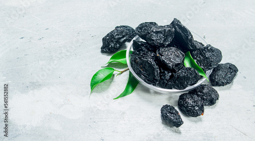 Prunes in a bowl with green leaves.
