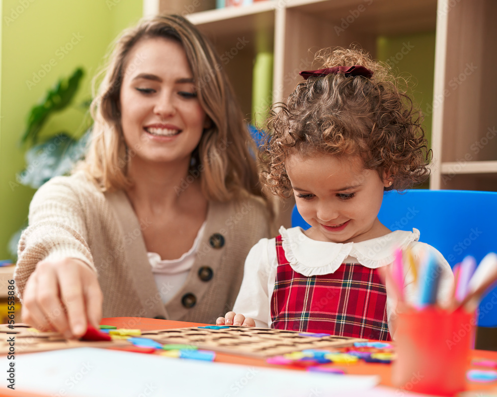 Fototapeta premium Teacher and toddler playing with maths puzzle game sitting on table at kindergarten