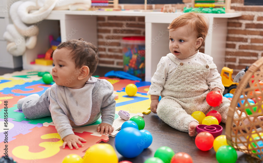 Two adorable babies playing with balls sitting on floor at kindergarten Two adorable babies playing with balls sitting on floor at kindergarten