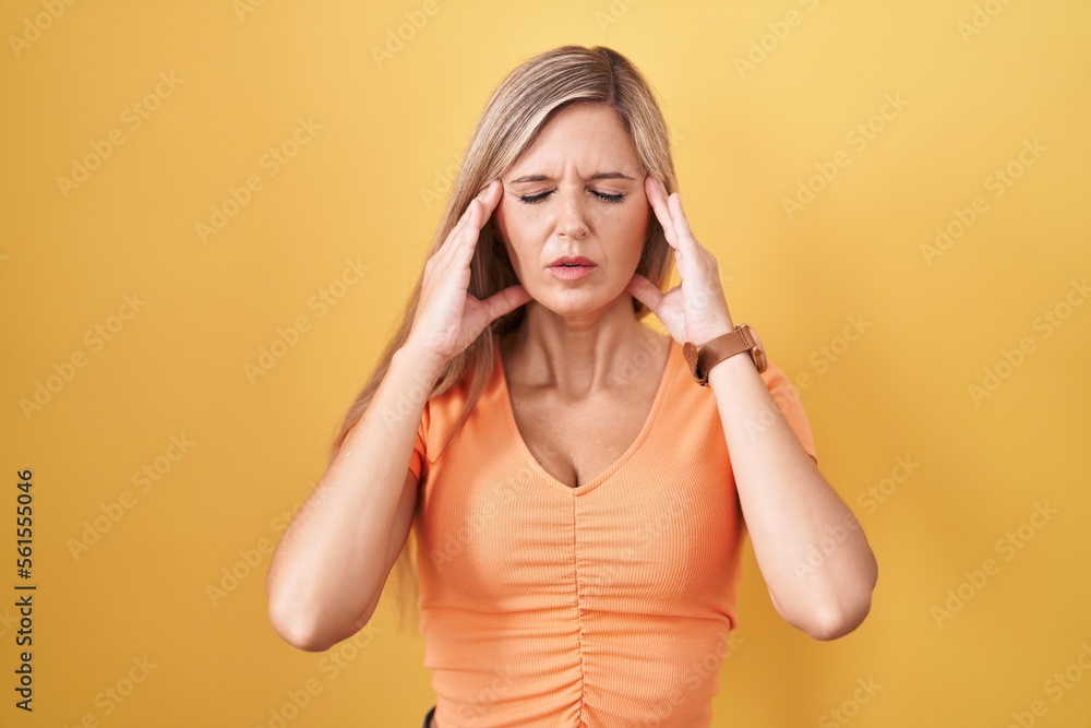 Young woman standing over yellow background with hand on head, headache because stress. suffering migraine. Young woman standing over yellow background with hand on head, headache because stress. suffering migraine.