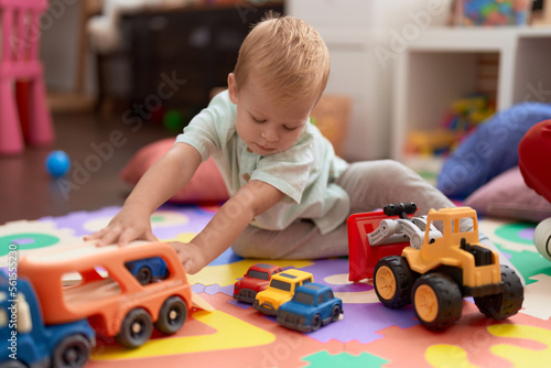 Adorable toddler playing with car toy sitting on floor at kindergarten
