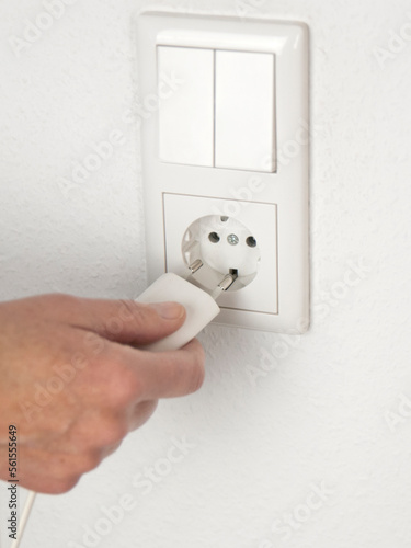 Strom und Energieverbrauch. Hand beim Einstecken eines weißen Steckers in die weiße Steckdose an der Wand