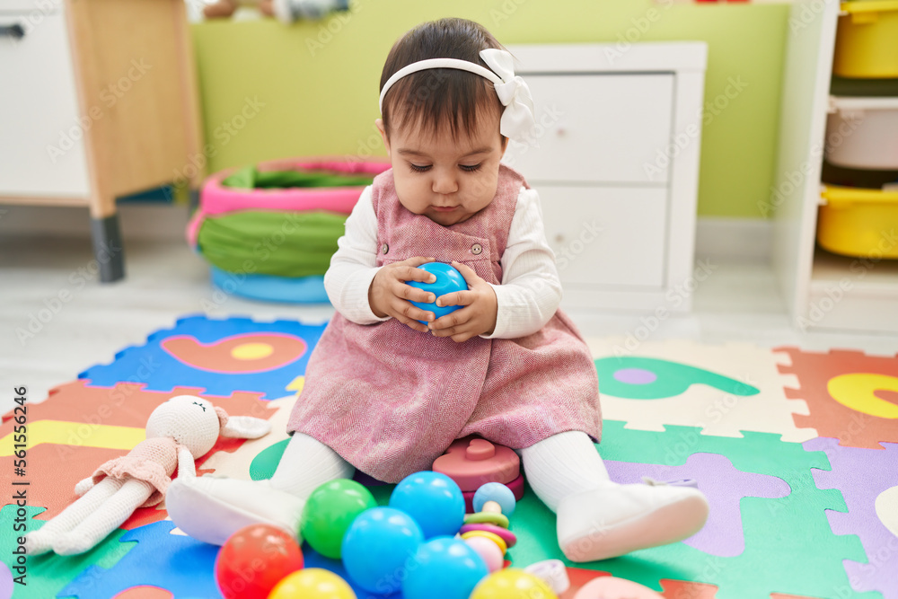 Adorable hispanic baby playing with balls sitting on floor at kindergarten Adorable hispanic baby playing with balls sitting on floor at kindergarten