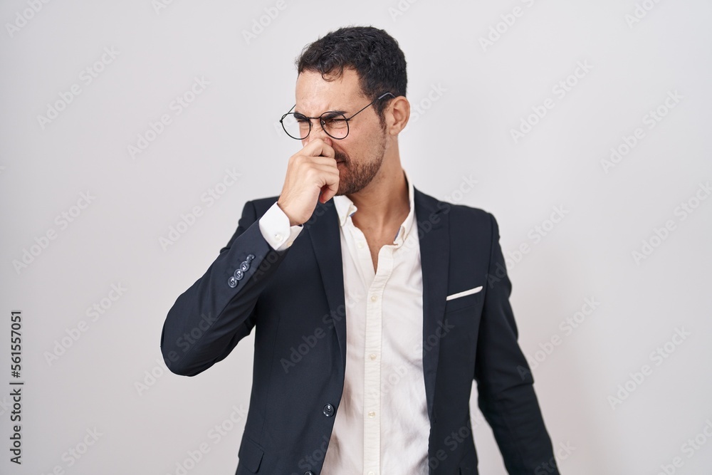 Handsome business hispanic man standing over white background smelling something stinky and disgusting, intolerable smell, holding breath with fingers on nose. bad smell Handsome business hispanic man standing over white background smelling something stinky and disgusting, intolerable smell, holding breath with fingers on nose. bad smell