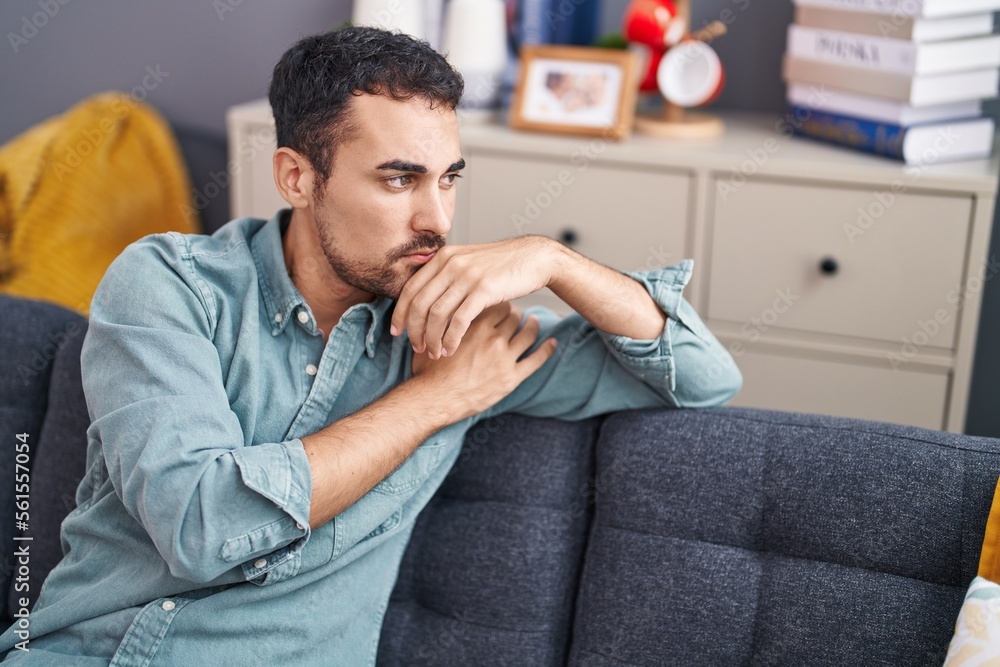 Young hispanic man sitting on sofa with serious expression at home Young hispanic man sitting on sofa with serious expression at home
