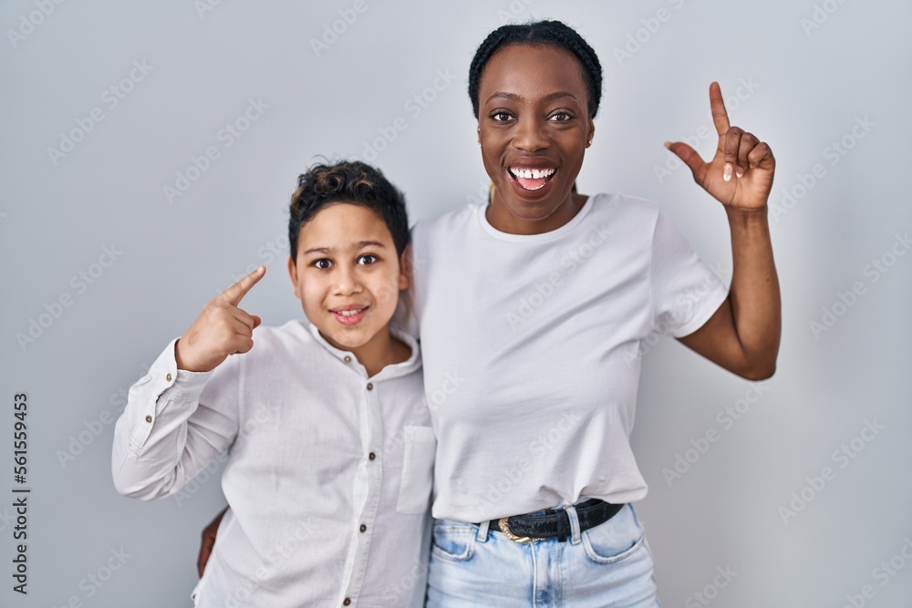 Fototapeta premium Young mother and son standing together over white background smiling amazed and surprised and pointing up with fingers and raised arms.
