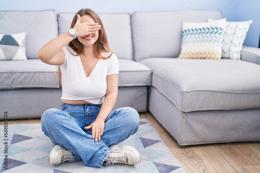 Young caucasian woman sitting on the floor at the living room smiling and laughing with hand on face covering eyes for surprise. blind concept. Young caucasian woman sitting on the floor at the living room smiling and laughing with hand on face covering eyes for surprise. blind concept.