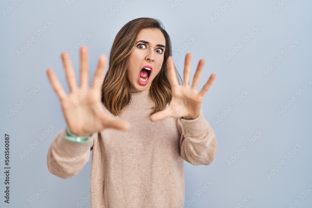 Young woman standing over isolated background afraid and terrified with fear expression stop gesture with hands, shouting in shock. panic concept. Young woman standing over isolated background afraid and terrified with fear expression stop gesture with hands, shouting in shock. panic concept.