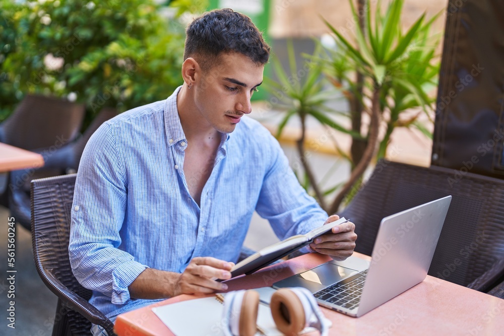Young hispanic man sitting on table studying at coffee shop terrace Young hispanic man sitting on table studying at coffee shop terrace