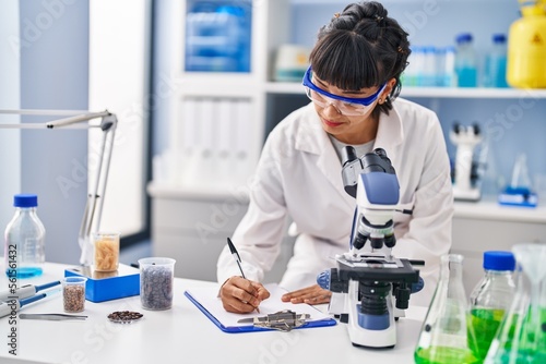 Young woman scientist writing on clipboard at laboratory