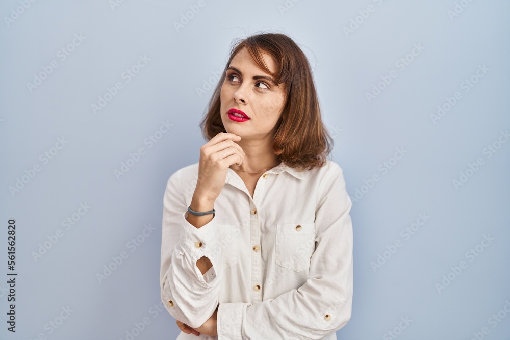 Young beautiful woman standing casual over blue background with hand on chin thinking about question, pensive expression. smiling with thoughtful face. doubt concept. Young beautiful woman standing casual over blue background with hand on chin thinking about question, pensive expression. smiling with thoughtful face. doubt concept.