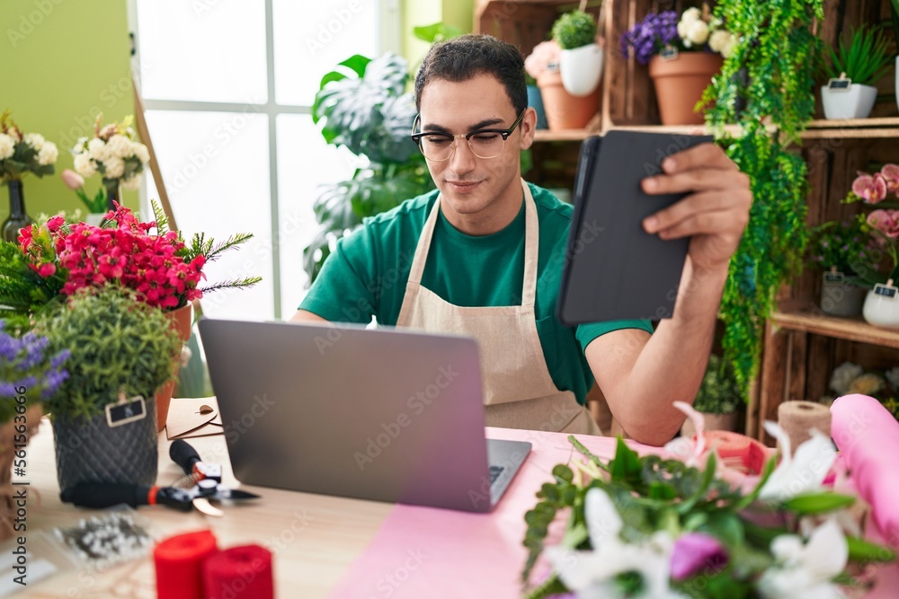 Young hispanic man florist using laptop and touchpad at flower shop