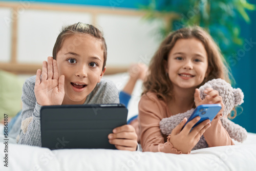 Two kids using smartphone and touchpad lying on bed at bedroom