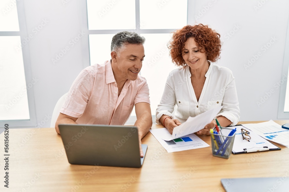 Middle age man and woman business workers using laptop and reading document at office Middle age man and woman business workers using laptop and reading document at office