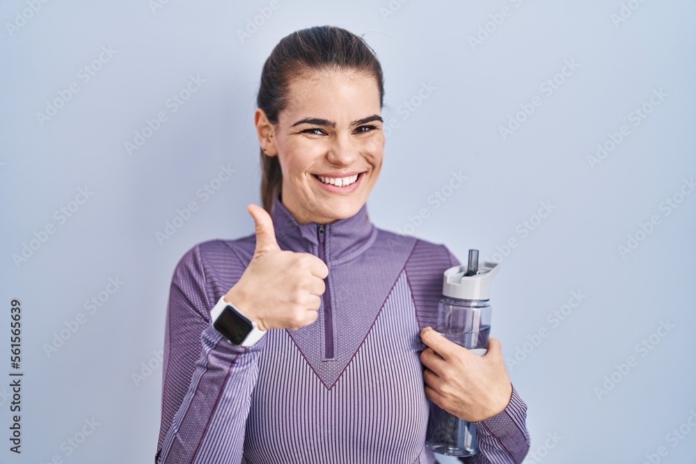 Beautiful woman wearing sportswear holding water bottle doing happy thumbs up gesture with hand. approving expression looking at the camera showing success. Beautiful woman wearing sportswear holding water bottle doing happy thumbs up gesture with hand. approving expression looking at the camera showing success.
