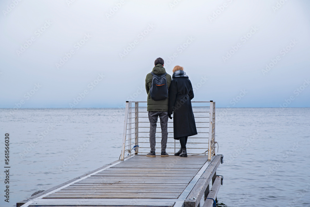 A couple in love by the sea on a cloudy day. Cold Baikal, a girl and a guy in warm clothes.