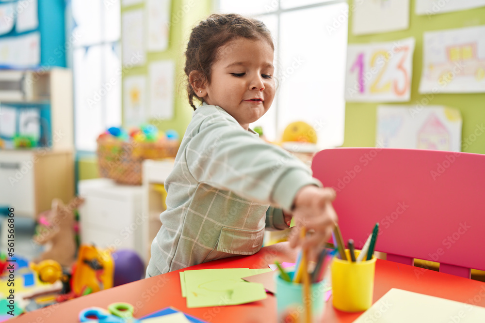 Adorable hispanic toddler student drawing on paper standing at kindergarten Adorable hispanic toddler student drawing on paper standing at kindergarten
