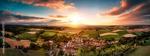 Aerial panorama of a village surrounded by fields at sunrise, with beautiful colorful sky and warm light