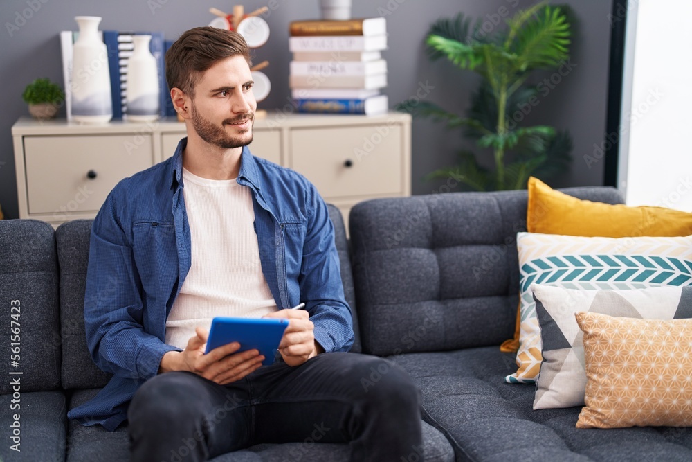 Obraz premium Young caucasian man using touchpad sitting on sofa at home