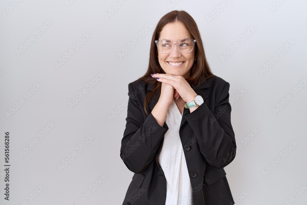 Beautiful brunette woman wearing business jacket and glasses laughing nervous and excited with hands on chin looking to the side Beautiful brunette woman wearing business jacket and glasses laughing nervous and excited with hands on chin looking to the side