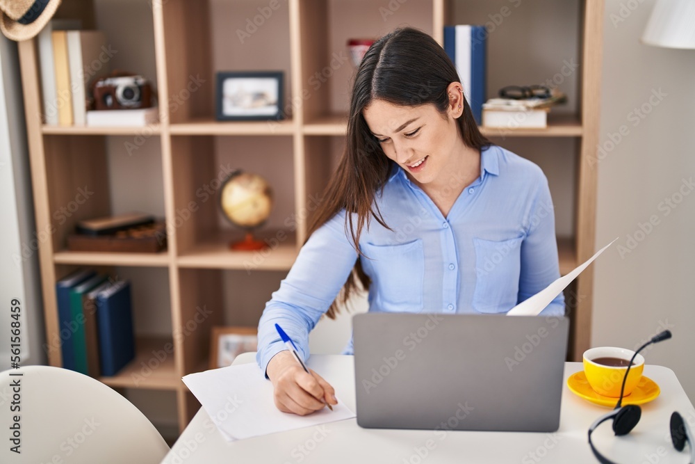 Young woman using laptop writing on document at home Young woman using laptop writing on document at home