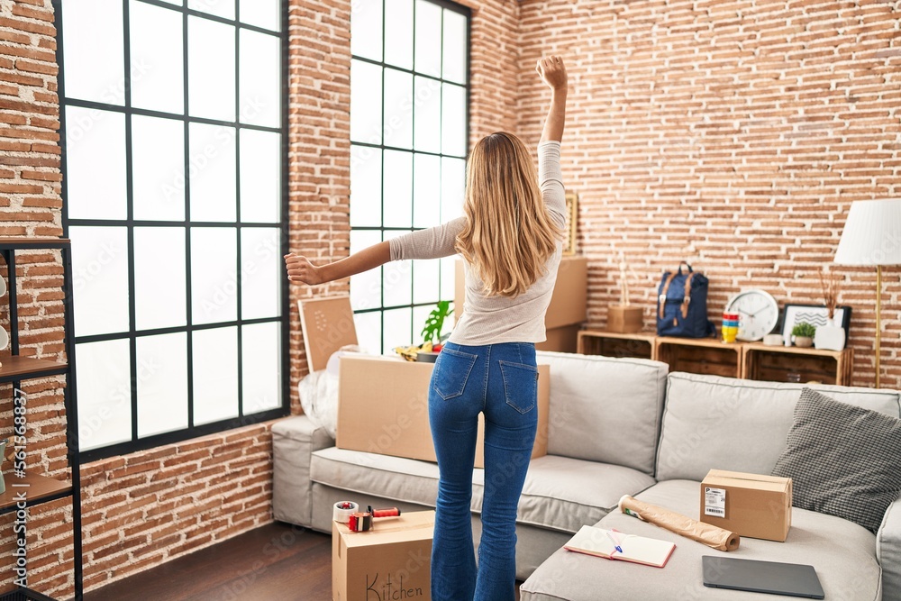 Young blonde woman on back view dancing at new home