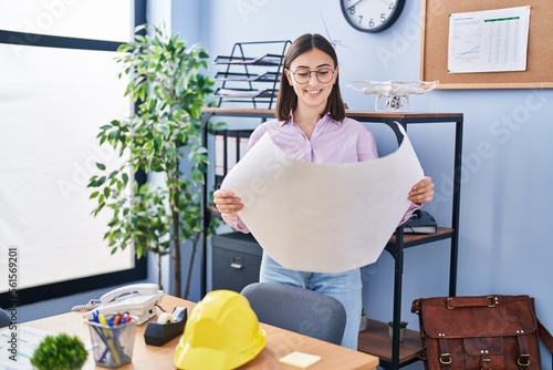 Young hispanic woman architect reading blueprints at office photo