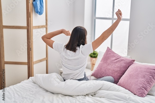 Young hispanic woman waking up sitting on bed at bedroom