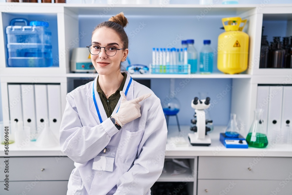 Young hispanic girl working at scientist laboratory smiling cheerful pointing with hand and finger up to the side Young hispanic girl working at scientist laboratory smiling cheerful pointing with hand and finger up to the side