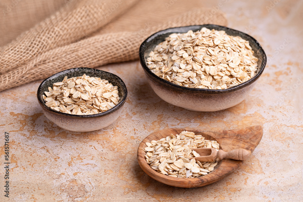 Oat flakes, cereal in handmade ceramic bowls and in a wooden bowl on burlap on a beige stone table, cereal scoop Oat flakes, cereal in handmade ceramic bowls and in a wooden bowl on burlap on a beige stone table, cereal scoop