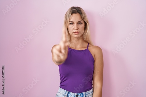 Young blonde woman standing over pink background pointing with finger up and angry expression  showing no gesture