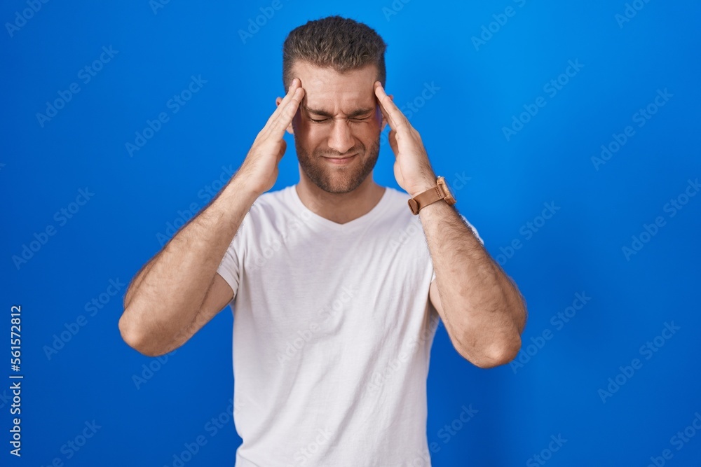 Young caucasian man standing over blue background with hand on head, headache because stress. suffering migraine. Young caucasian man standing over blue background with hand on head, headache because stress. suffering migraine.